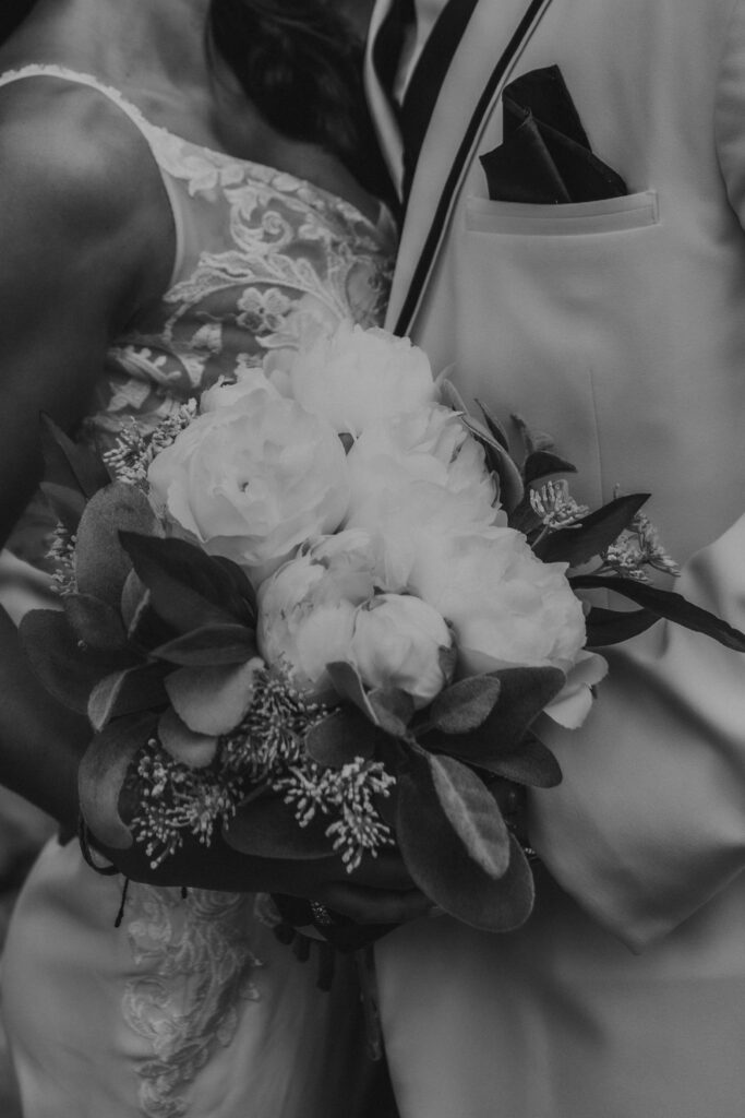 black and white wedding photo of the details of florals, lacey wedding dress, white tux