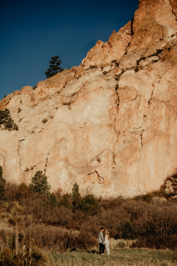 "Nick kneeling to propose to Callie on a quiet trail at Garden of the Gods, captured from a distance with a telephoto lens."