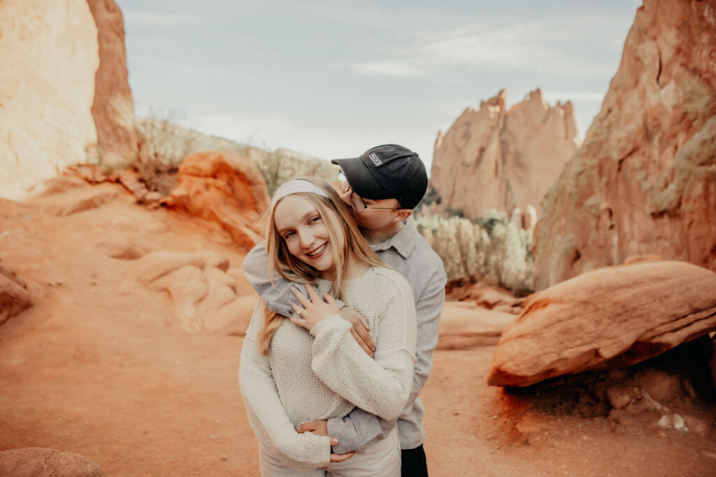 Callie and Nick embracing joyfully after the proposal, with the red rock formations of Garden of the Gods in the background