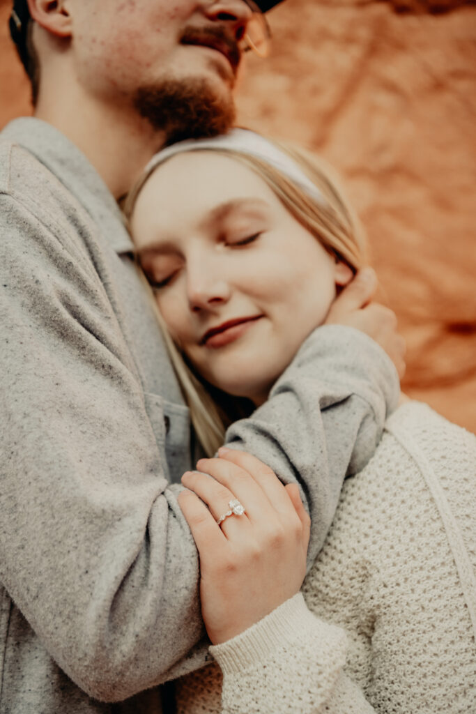 Nick holding onto Callies neck as she rests her head on his chest with them blurry and the ring in focus