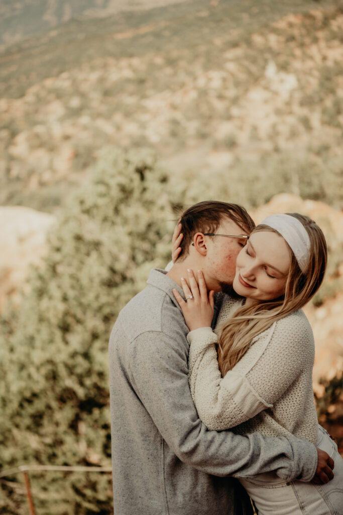 Callie and Nick embracing joyfully after the proposal, with the red rock formations of Garden of the Gods in the background