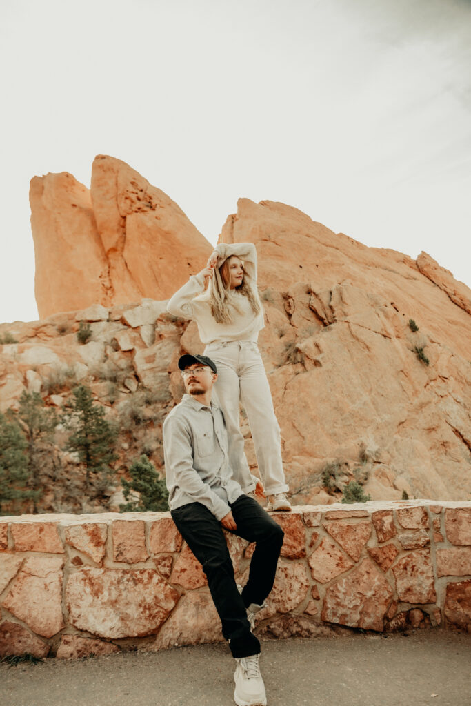 Callie standing on the brick wall striking a pose with her hands about her head and Nick sitting down on the brick wall. As they both look in opposite directions. 