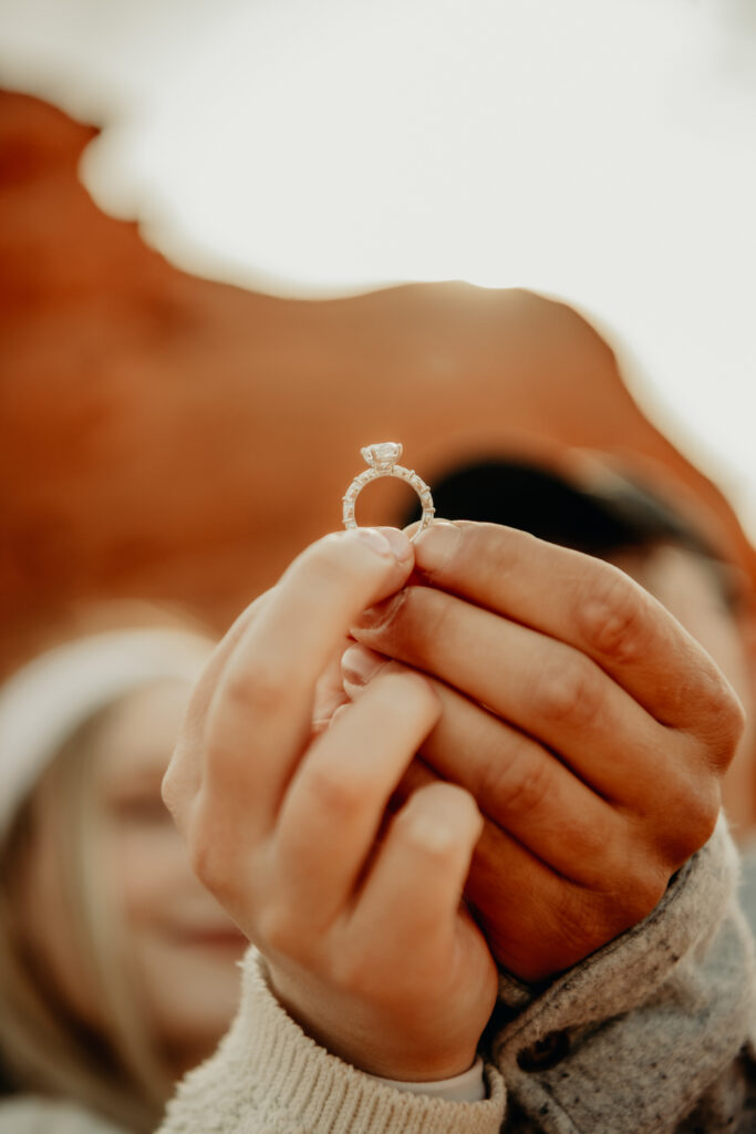 Nick and Callie holding the engagement ring to show off the details as they are blurred in the background