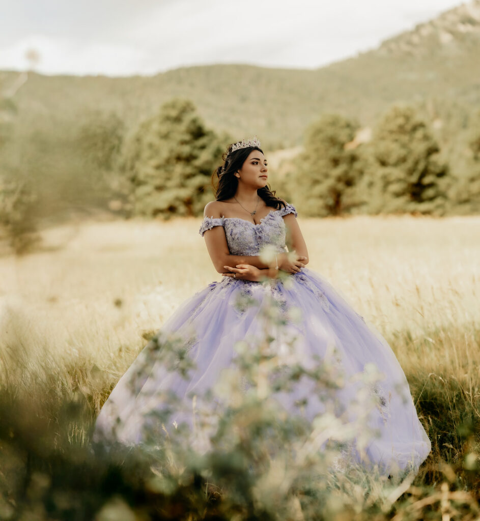 Quinceañera portrait of Natalia in a lavender purple ball gown standing with a tiara in an open field in Evergreen, Colorado
