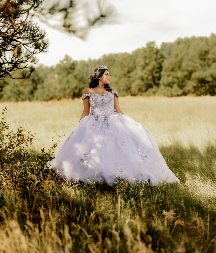 Quinceañera portrait of Natalia in a lavender purple ball gown standing with a tiara in an open field in Evergreen, Colorado
