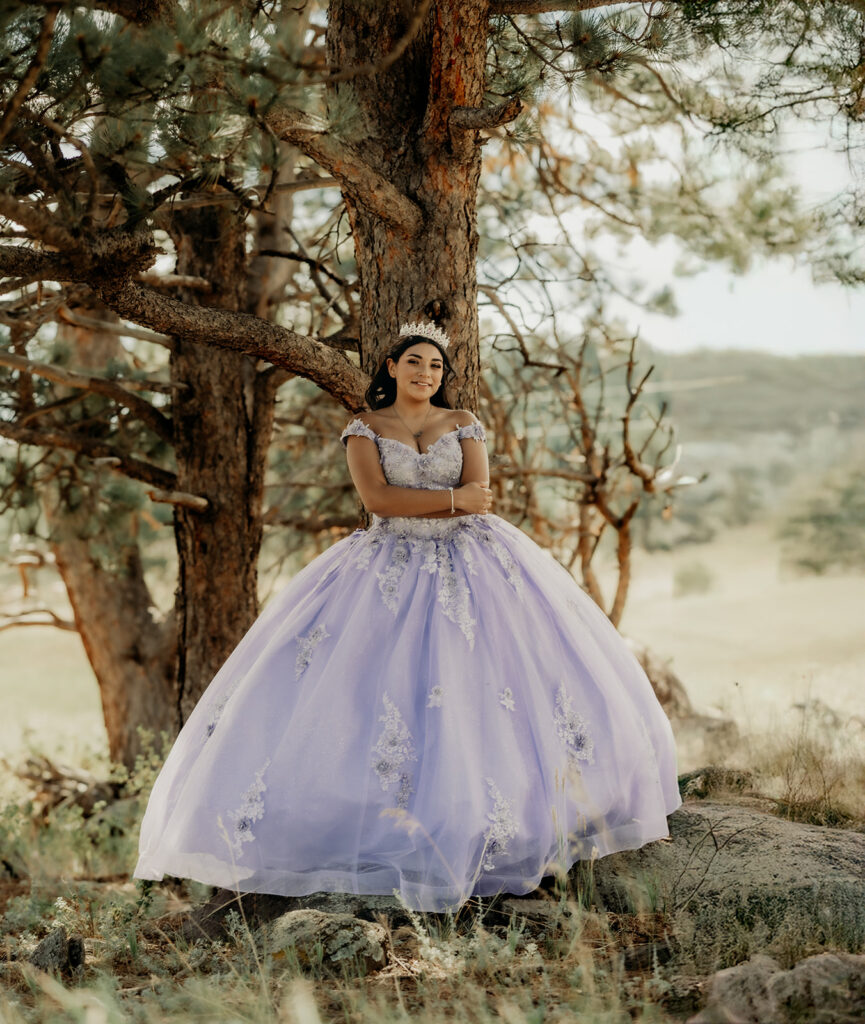 Quinceañera portrait of Natalia in a lavender purple ball gown standing with a tiara in an open field in Evergreen, Colorado