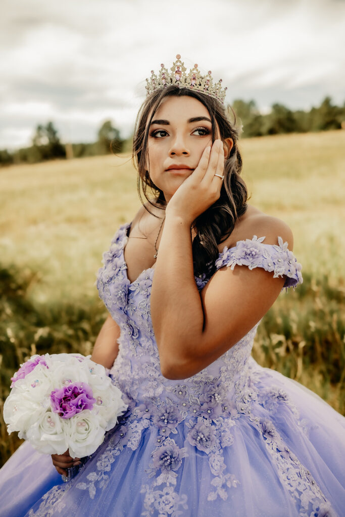 Quinceañera portrait of Natalia in a lavender purple ball gown standing with a tiara in an open field in Evergreen, Colorado