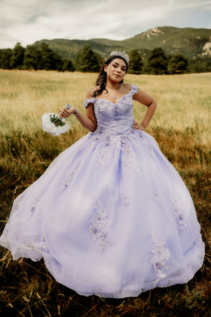 Quinceañera portrait of Natalia in a lavender purple ball gown standing with a tiara in an open field in Evergreen, Colorado