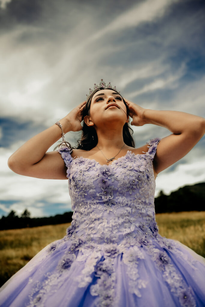 Quinceañera portrait of Natalia in a lavender purple ball gown standing with a tiara in an open field in Evergreen, Colorado