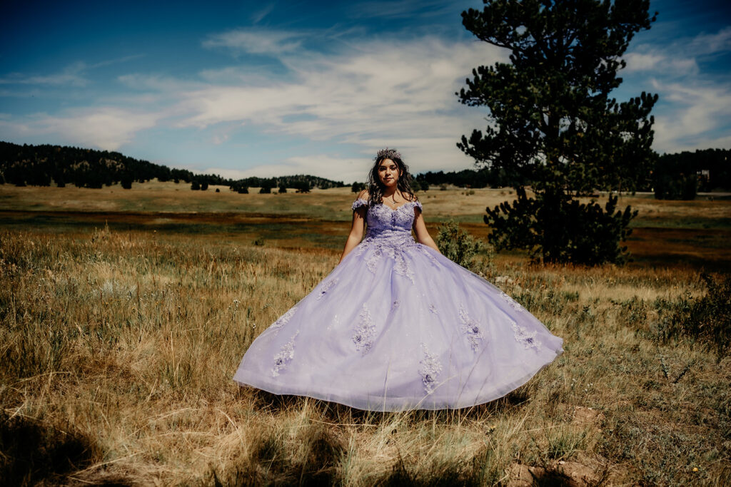 Quinceañera portrait of Natalia in a lavender purple ball standing in an open field in Evergreen, Colorado