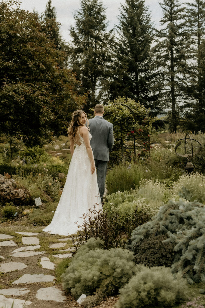 groom leading the way down the pathway at the  Yampa River Botanic Gardens as the bride looks over her shoulder- what a model!