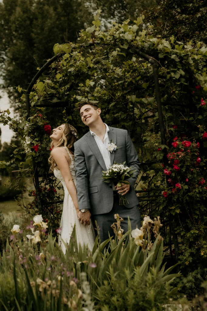 sweet laughter and candid moments from the bride and groom under the floral archway in June at the Yampa River Botanic Gardens