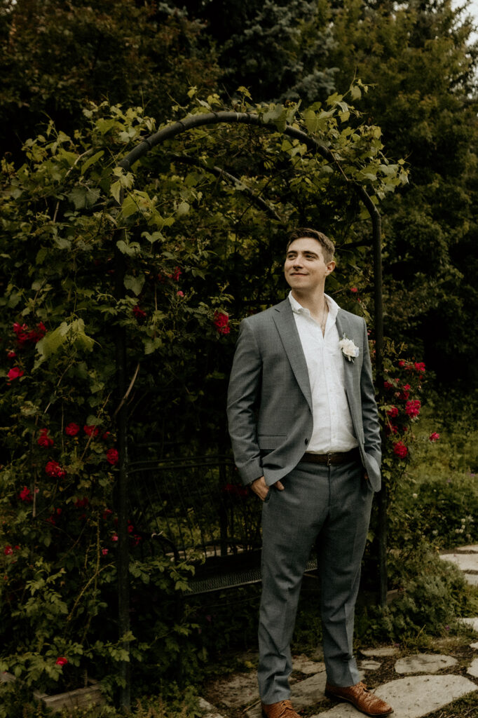 the groom standing like a handsome gentlemen under the floral archway at the Yampa River Botanic Gardens