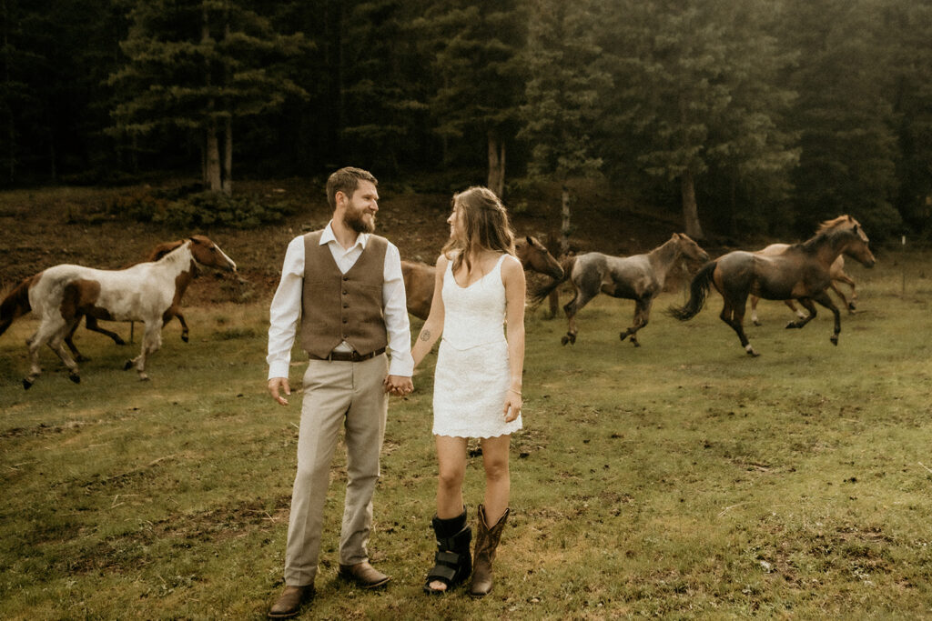 newly weds holding hands looking at each other as horses run behind them